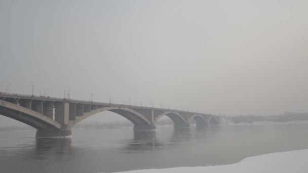 Straßenbrücke über einen Fluss im winterlichen Russland. Sibirischer Frost. Fluss mit Eis bedeckt. sehr kaltes Wasser in der sibirischen Stadt. Schwierige klimatische Bedingungen. — Stockvideo