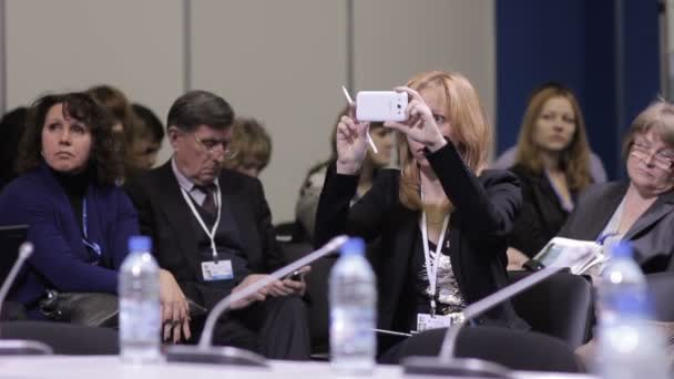 Åskådarna sitter i möte av det internationella ekonomiska forumet. Noggrant lyssna till talare tala mycket viktiga saker. Flicka fotografier på telefonen. — Stockvideo