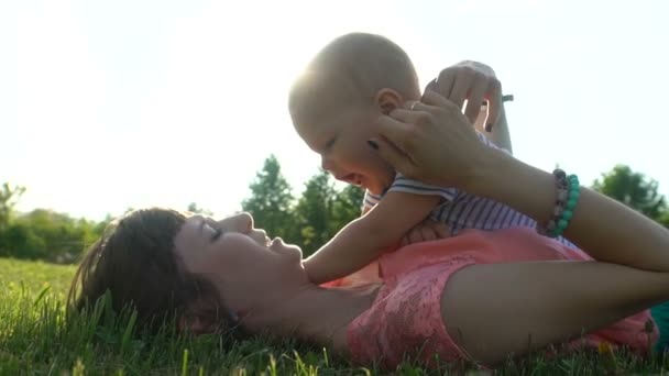 Молодая счастливая мать с ребенком, лежащим и отдыхающим на зеленой лужайке в парке — стоковое видео