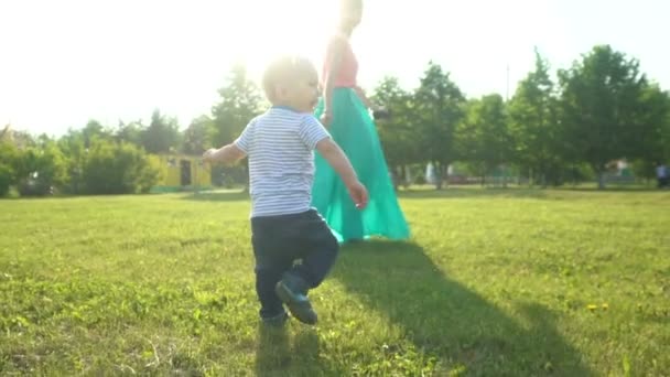 Een gelukkig kind draait voor zijn geliefde moeder op groen gras in het park. — Stockvideo