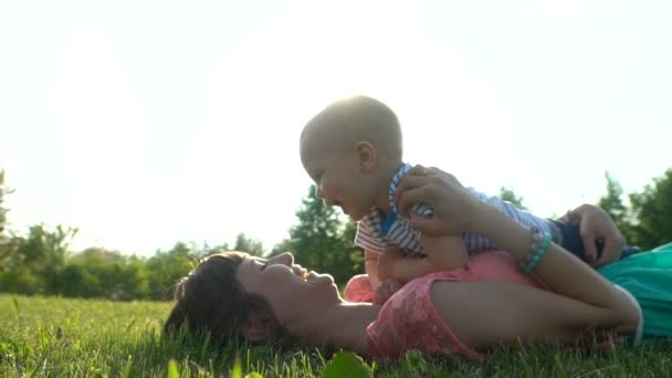 Joven madre feliz con un niño acostado y descansando en un césped verde en un parque — Vídeos de Stock