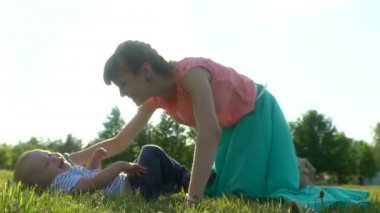 Yalan ve bir parkta yeşil bir Çimenlikte oturan bir çocuk ile genç mutlu anne