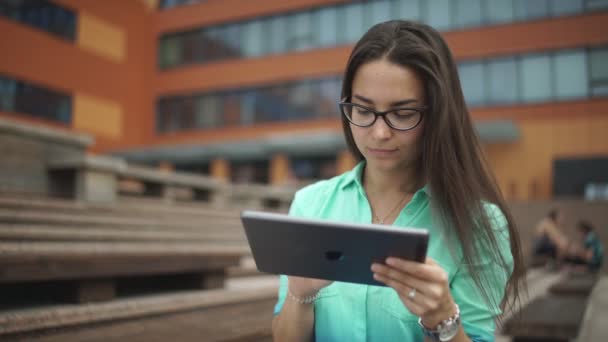 Hermosa estudiante con una tableta digital sentada en el espacio abierto . — Vídeo de stock