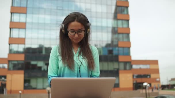 Joven hermosa chica sentada con un ordenador portátil y auriculares — Vídeo de stock