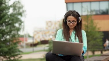 Kulaklıkla müzik dinleyen ve dizüstü bilgisayar klavyesi üzerinde yazan kız