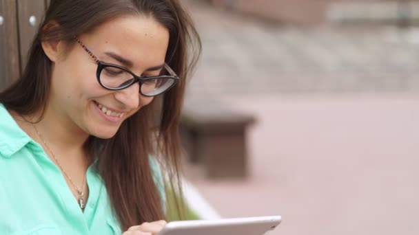 Estudiante alegre en gafas con una tableta digital sentado — Vídeo de stock