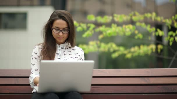 Elegante jonge vrouw zitten met een laptop buitenshuis. Extern werk. — Stockvideo