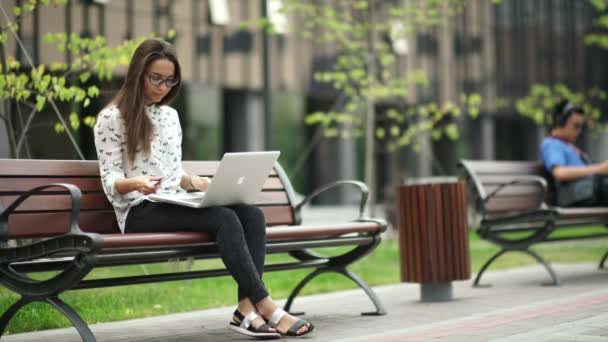 Beautiful girl with a laptop sitting on the street. Remote work. — Stock Video