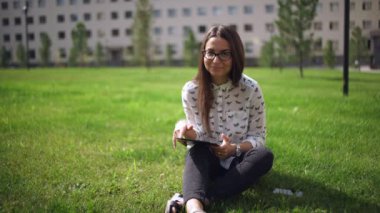 Çimenlerin üzerinde oturan dijital tablet ile gözlük güzel öğrenci