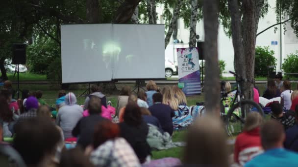 Россия, Новосибирск, 2016: люди сидят на траве и смотрят кино — стоковое видео