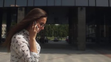 Uzun saçlı kız sokakta sallanıp telefonda konuşuyor.