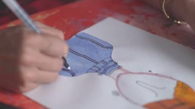 Sanatçının elinde keçeli kalem. Masaya çizim.