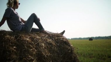 Young stylish girl in a striped t-shirt sitting on a haystack.