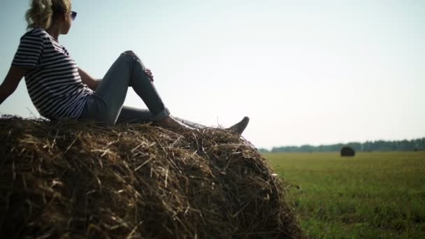 Young stylish girl in a striped t-shirt sitting on a haystack. — Stok video