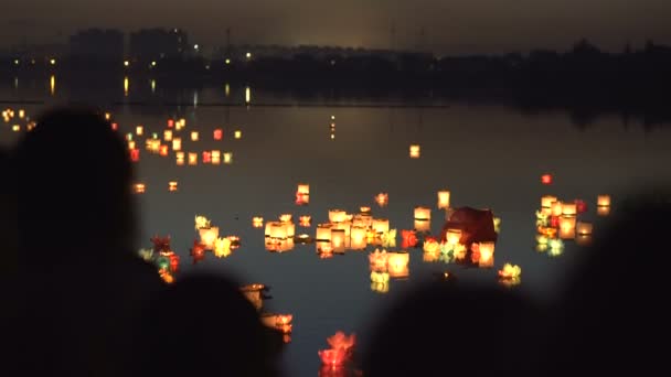 Silhouette di persone sulla riva del fiume. La gente guarda le lanterne dell'acqua . — Video Stock
