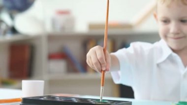 Sarı saçlı çocuk suluboya boyası yapıyor. Çocuk bir ağrı fırça dunks