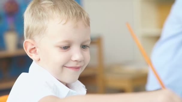 Το πορτραίτο ενός χαριτωμενο αγοριού με ξανθά μαλλιά. Το αγόρι ζωγραφίζει με χρώματα. — Αρχείο Βίντεο