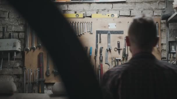 Centro de servicio: mecánico se acerca a la pared con herramientas, toma una llave — Vídeos de Stock