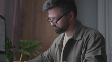 Bir adam çalışıyor, bir ofis masasında oturuyor ve kalemle yazıyor.