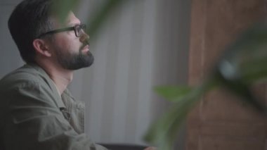 Gözlüklü, sakallı bir adam ev ofisinde çalışıyor.