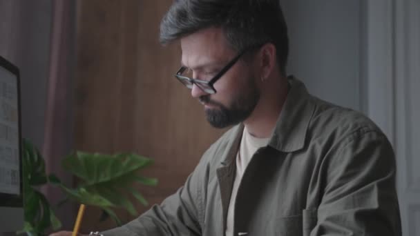 Un hombre trabaja, se sienta en una mesa de oficina y escribe con un lápiz — Vídeo de stock