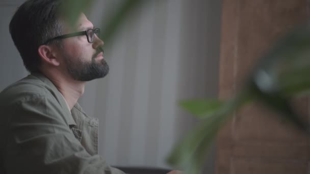 Человек в очках с бородой работает в домашнем офисе — стоковое видео