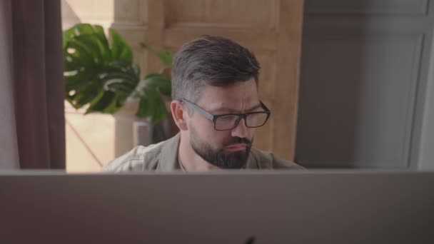 El hombre paga las facturas sentado frente a la computadora en el interior del hogar — Vídeos de Stock