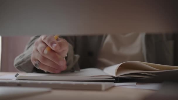 Mężczyzna pisze ręcznie w notesie, siedząc przed komputerem.. — Wideo stockowe