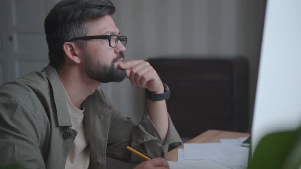 En mann sitter på et hjemmekontor og fyller ut forretningsdokumenter – stockvideo