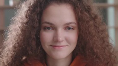 Kıvırcık kız öğrenci kameraya bakar ve gülümser. Kapat, gün ışığı.