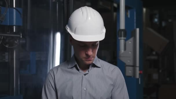 Trabajador en la producción moderna: un joven ingeniero exitoso en un casco blanco y camisa hace el control de calidad. — Vídeo de stock