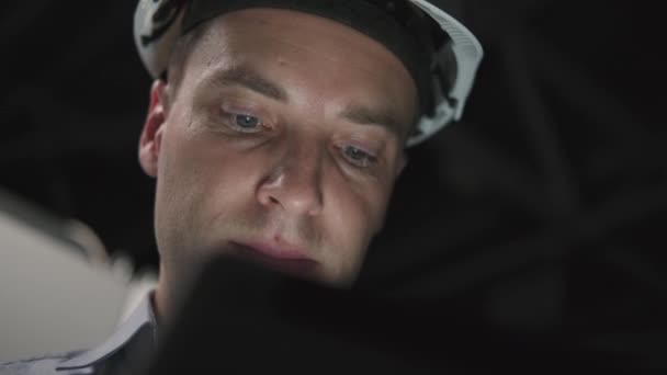 El rostro de un hombre en un casco iluminado por una tableta — Vídeos de Stock