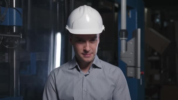 Een ingenieur met een witte helm kijkt naar beneden, rijgt zijn hoofd en glimlacht — Stockvideo