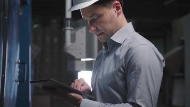 Ingeniero masculino en camisa y casco comprueba el dispositivo en producción — Vídeos de Stock