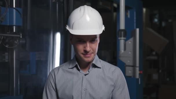 Un profesional masculino en un casco y una camisa casual en una producción. — Vídeos de Stock