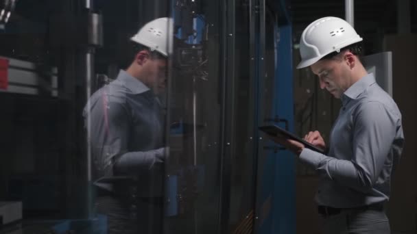 Инженер в рубашке и шлеме проверяет устройство. — стоковое видео
