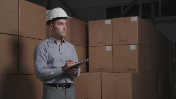 O funcionário de armazém no capacete branco duro executa uma auditoria. — Vídeo de Stock