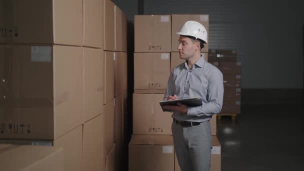 A man works in a warehouse with cardboard boxes, makes an inventory. — Stock Video