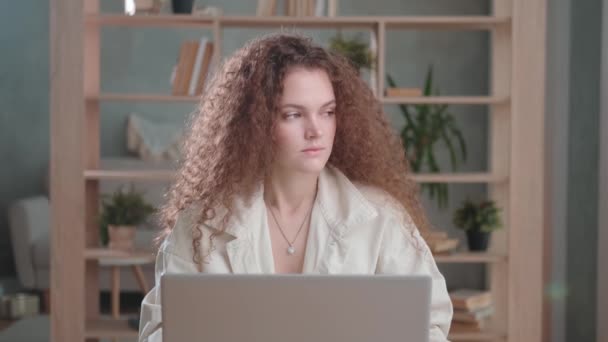 Mujer con el pelo largo y rizado con un ordenador portátil, mirando cansada a un lado — Vídeos de Stock