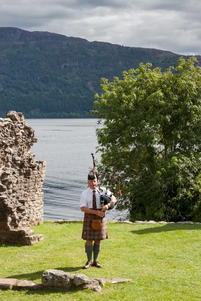 Scottish Highlander wearing kilt and playing Bagpipe at Urquhart Castle — Stock Photo, Image