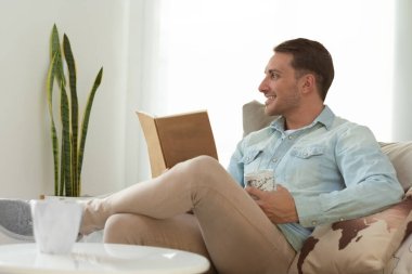 Genç adam pencereden dışarı bakıyor, elinde bir kitap tutuyor.