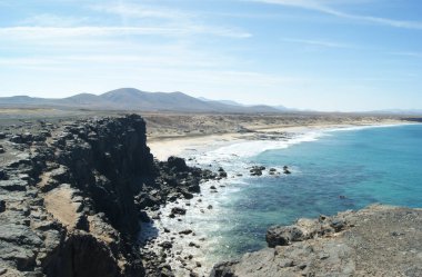 Fuertevenura İspanya. Dramatik, güzel manzara. Deniz, kayalıklar ve sahil. El Cotillo 'nun küçük balıkçı kasabasının oradaki el değmemiş kumsalda dalgalar kopuyor. Mavi gökyüzü ve alanı kopyala.
