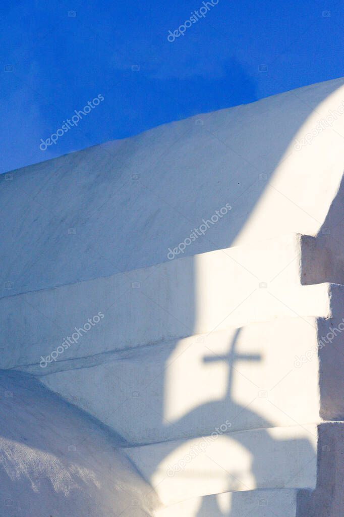 Greek island church, Ios island. Close up view of elegant old building.  Shadow of a cross on the chapel, from a bell tower. Blue sky and copy space. 