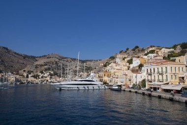 Symi Adası Yunanistan. Güzel teknelerle dolu dramatik bir liman. Açık mavi gökyüzü ve boşluğu kopyalayan manzara görüntüsü. Geleneksel neo klasik evler rıhtıma dizilir. 