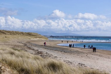 Rhosneigr köyü, Anglesey Wales. Kumsal manzaralı güzel kumlu bir sahilin üzerinde dalgalar kumsala çarpıyor. Bahar gününde güzel bir deniz manzarası. Mavi gökyüzü, manzara ve kopyalama alanı.  