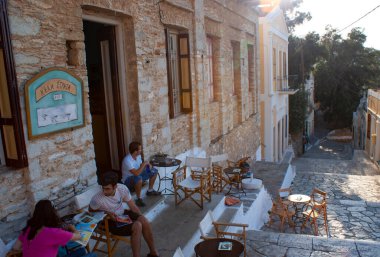 Yunanistan, Symi Adası 'nda küçük bir bar. Turistler gölgeli bir terasta rahatlar, içkinin tadını çıkarırlar. Peyzaj görünümü.