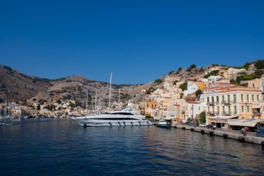 Symi Adası, Yunanistan. Liman manzarası. Güzel liman cephesi boyunca demirlemiş renkli teknelerin olduğu dramatik bir liman manzarası. Mavi gökyüzü ve boşluk kopyala.  