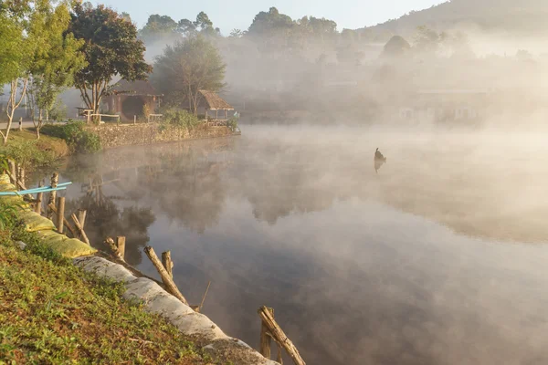 Köyün şafakta sakin suda yansıyan bulutlu sis