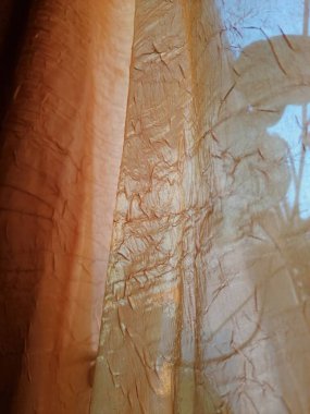 Güzel turuncu perde. arka plan dokusu. Altın rengi bir perde. Sarı turuncu. Pencerede tül var. Güneş, tülün dokusuyla oynar ve pencereden içeri doğru parlar. Yarı saydam tül perdesi