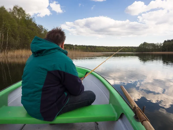 Bir sandalda oturan ve bir gölde balıkçılık tarafından boş zaman harcama adam